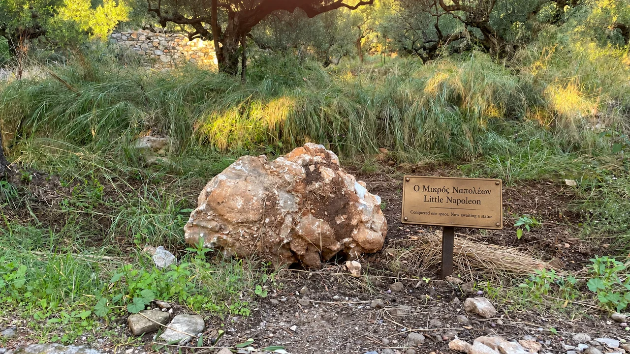 Μικρή στρογγυλεμένη πέτρα στο γρασίδι, με ψηφιακά προστιθέμενη μουσειακή πινακίδα