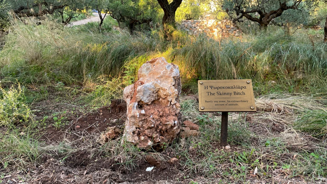 Στενή όρθια πέτρα σε χώμα, με ψηφιακά προστιθέμενη μουσειακή πινακίδα